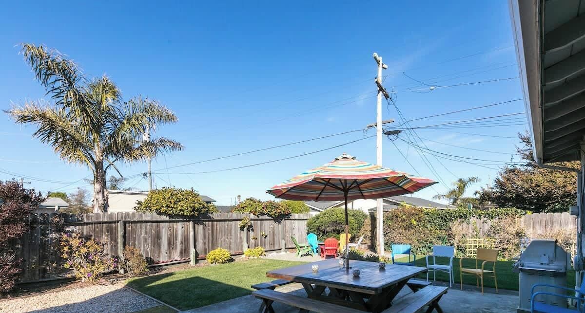 A backyard with a picnic table, a colorful umbrella, and a wooden fence.