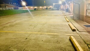 Un estacionamiento con espacios delimitados y un edificio con puerta de garaje.