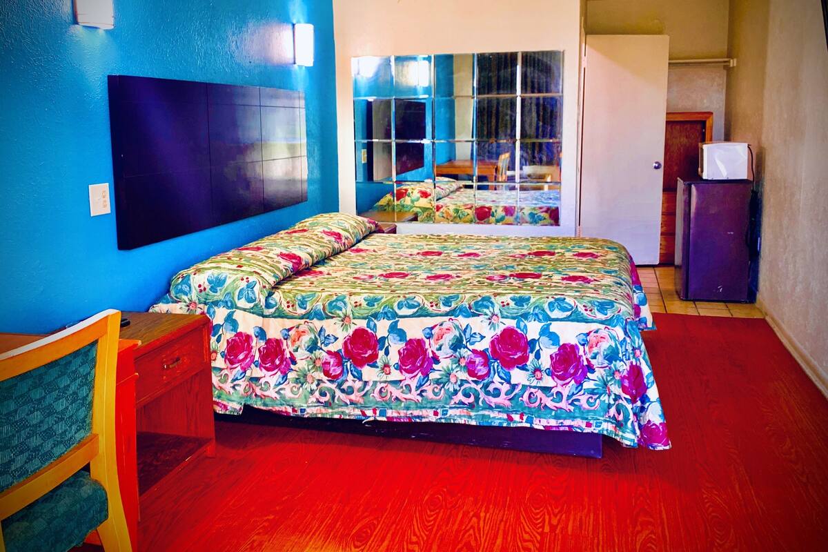 A room with two beds, a wooden chair, a small table, and a refrigerator.