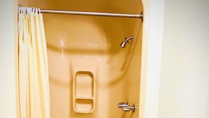 Una bañera pequeña y cerrada con cortina de ducha, un grifo y un inodoro a la vista a través de una puerta abierta.