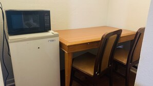 Una kitchenette compacta con microondas, un refrigerador pequeño, una mesa de madera y dos sillas.