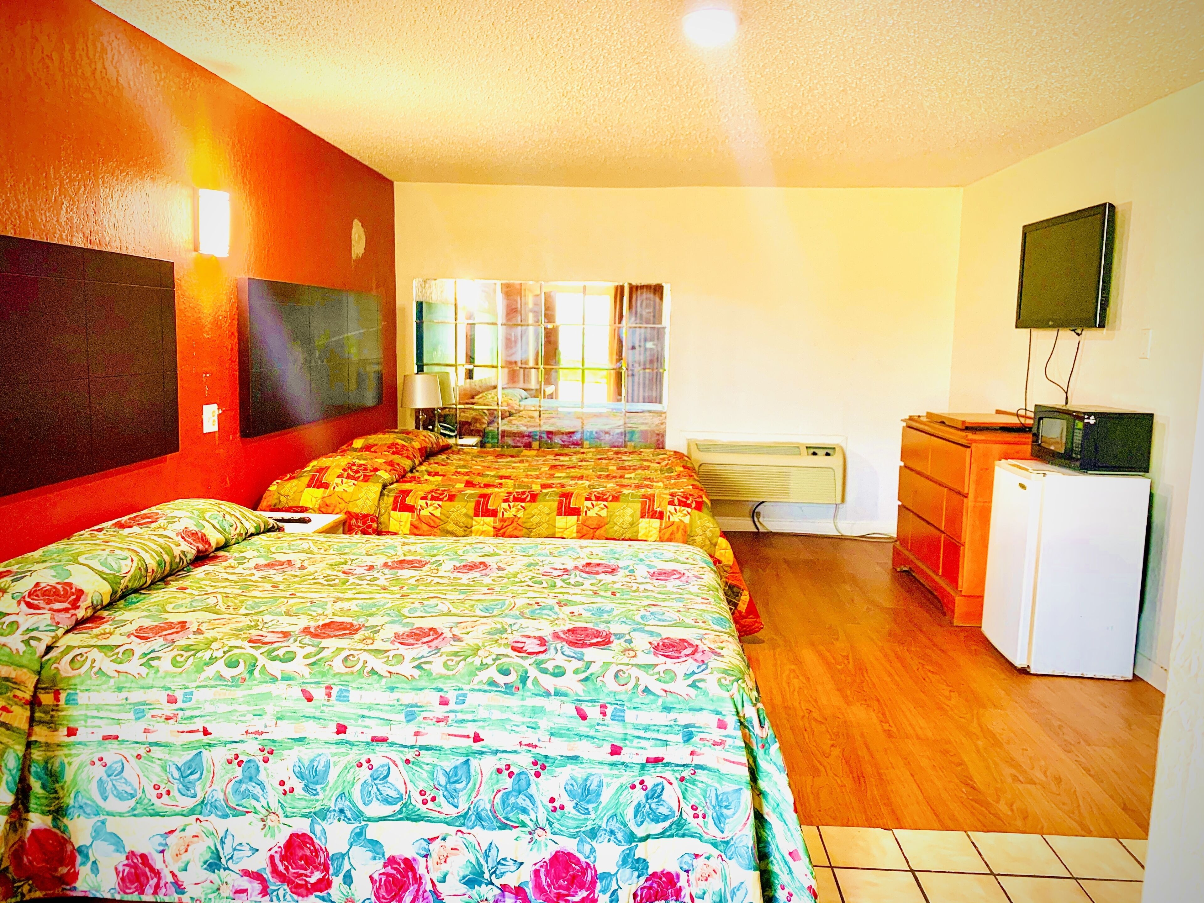 A hotel room with two beds, a television, a refrigerator, and a window with curtains.