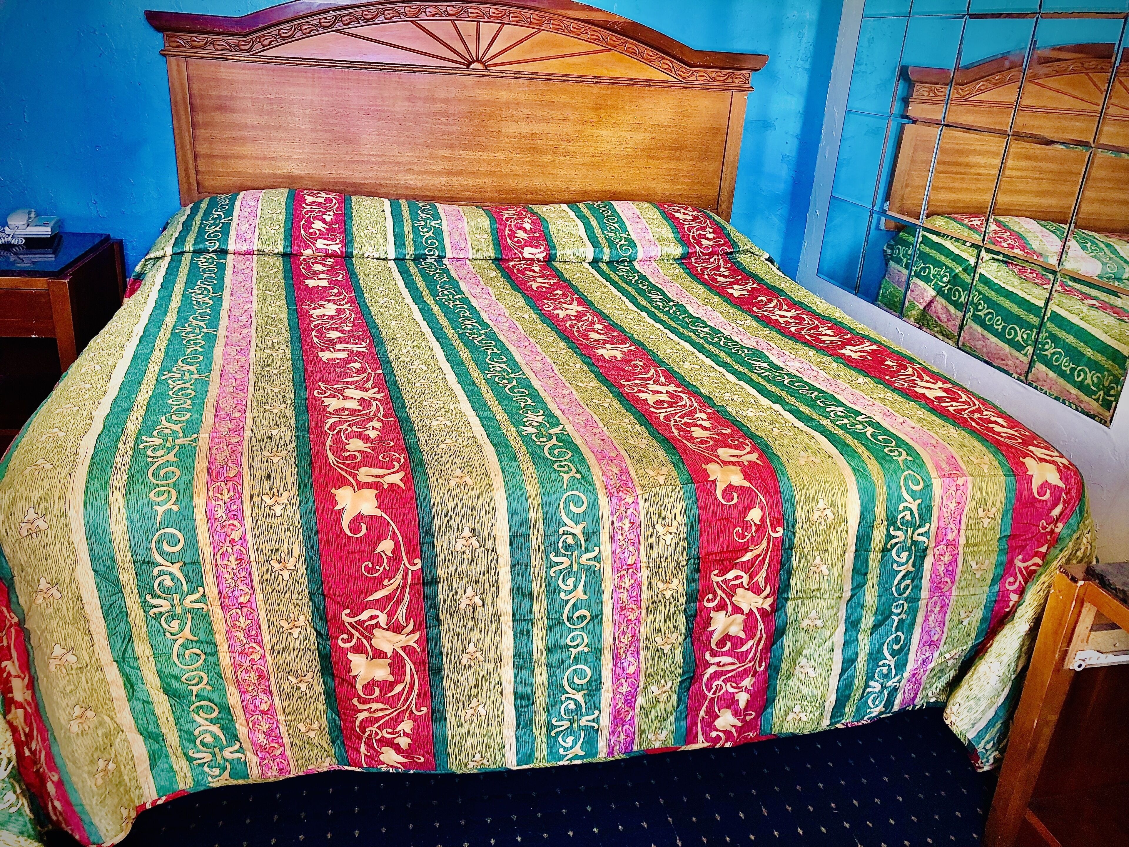 Una cama con una colcha a rayas de colores y un cabecero de madera.