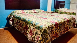 Un dormitorio con colcha estampada de flores, cabecero oscuro y un espejo grande en la pared.