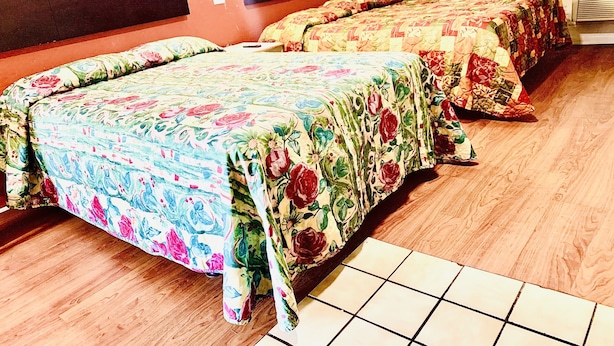Habitación de hotel con dos camas, cada una con ropa de cama floral, suelo de madera y ventana con vistas.
