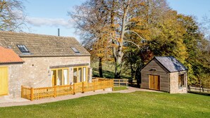 Ein Steinhaus mit Holzzaun, einer kleinen Werkstatt und einem Rasen.