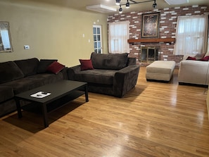 Relax in this stylish living room with a sofa, armchair, and ottoman, surrounded by a brick accent wall and a large framed picture above the fireplace.