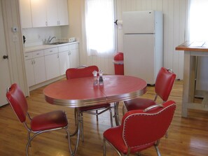 Une cuisine de taille réduite avec des meubles blancs, une table ronde rouge et des chaises assorties, également rouges.
