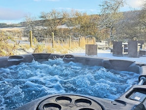 Ein Whirlpool, umgeben von einer Holzterrasse und Gartenmöbeln, mit einer natürlichen Landschaft im Hintergrund.