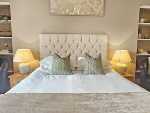 A neatly made bed with a tufted headboard, two bedside lamps, and two patterned pillows. - 4 bedroom accommodation in Scaniport, near Inverness (Scaniport, near Inverness)