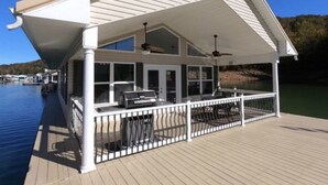 Une terrasse extérieure couverte, équipée d’un barbecue et d’un espace salon, avec vue sur une étendue d’eau.