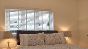 A neatly made bed with floral bedding, two bedside lamps, and a window with blinds. - 1 bedroom accommodation in Hawley (Hawley)