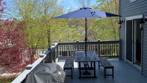 Eine überdachte Terrasse im Freien mit Grill, Picknicktisch und Sonnenschirm.