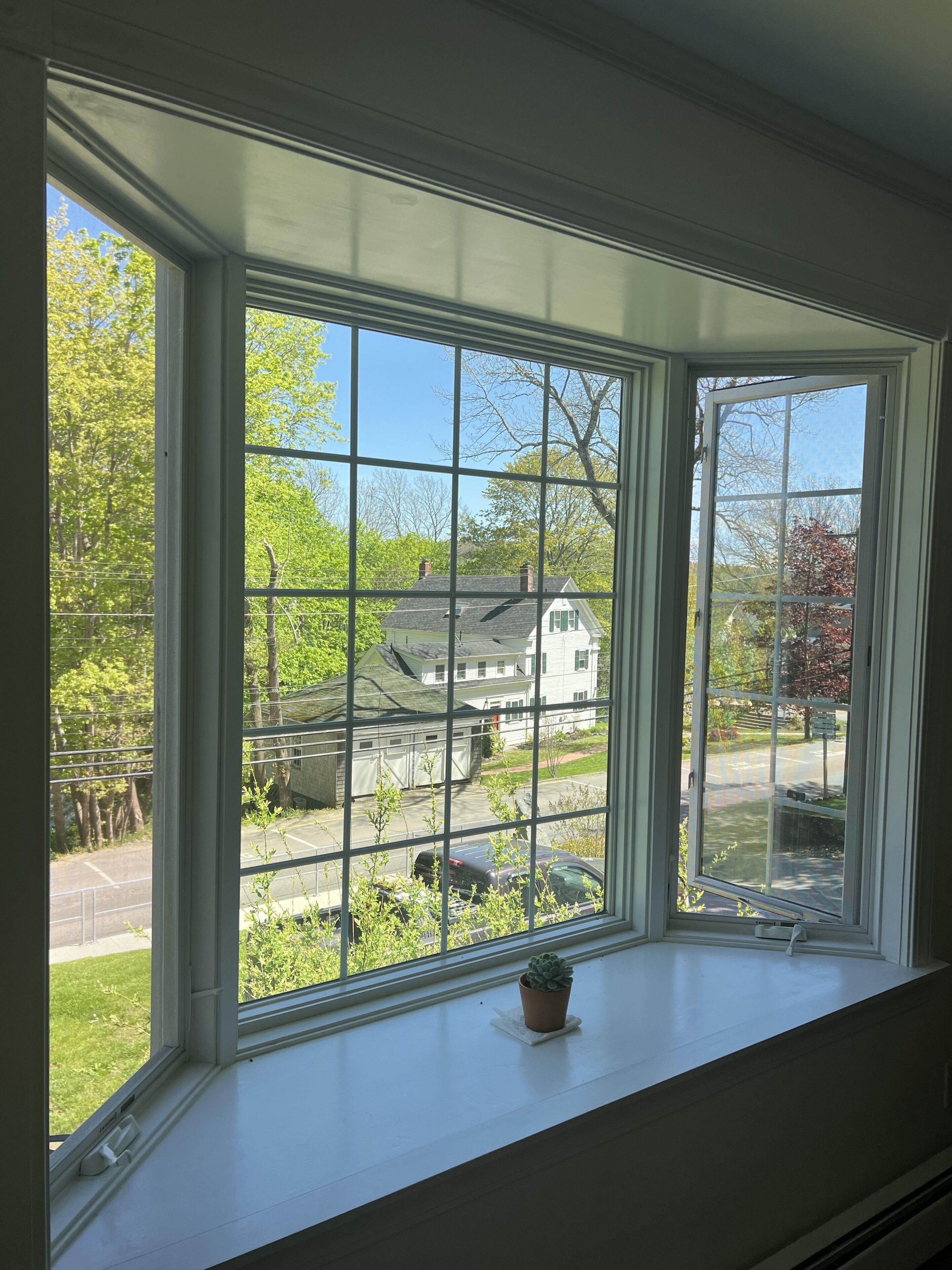 A bay window with a clear view of a residential area, including houses and greenery.