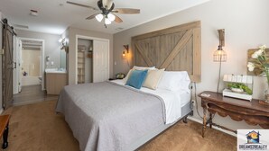 Ein Schlafzimmer mit Bett, Deckenventilator, Nachttisch mit Lampe und Holz-Kopfteil.