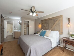 Une chambre à coucher avec un lit, un ventilateur de plafond, une table de chevet avec une lampe et une tête de lit en bois.