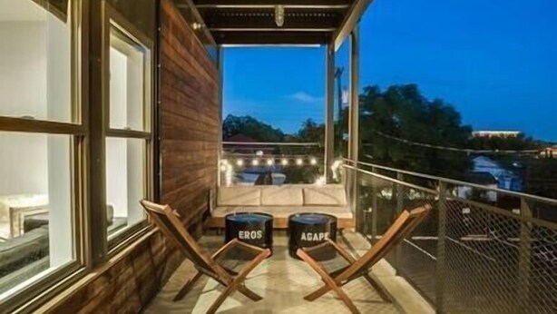 Ein Balkon mit Blick auf die Stadt im Abenddämmerung, mit Holzboden, zwei Loungestühlen und einem kleinen Tisch.