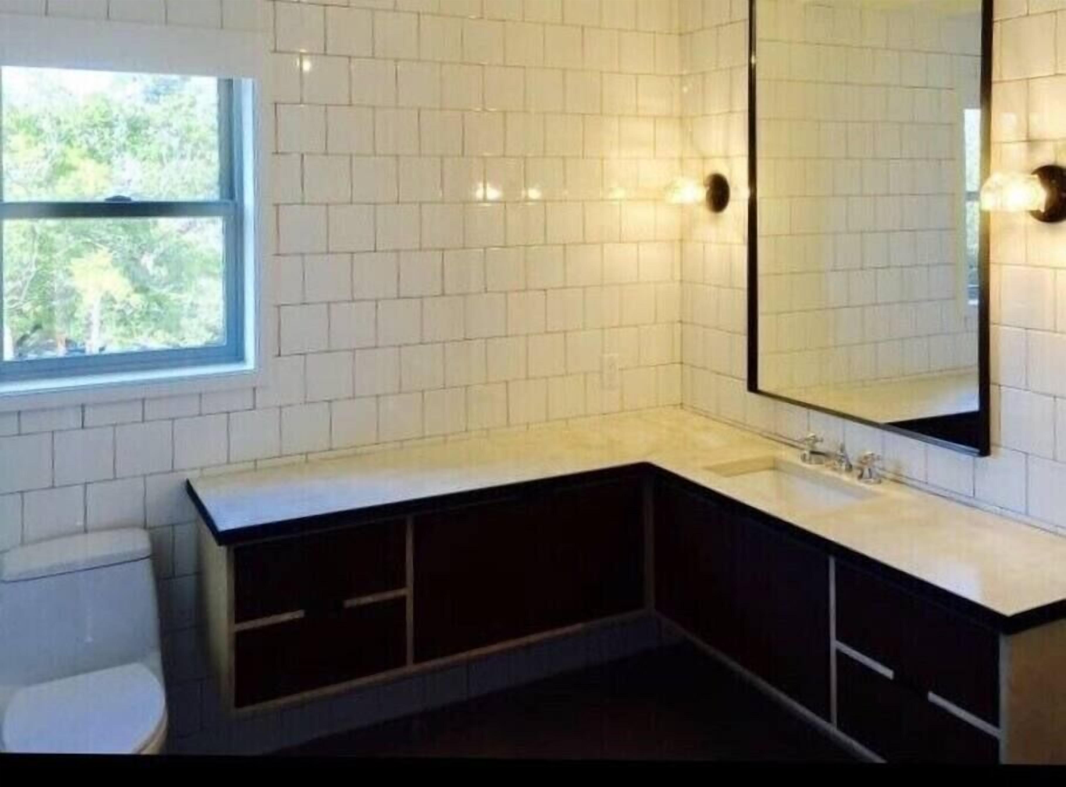 A modern bathroom with white tiles, a large mirror, a sink, and a toilet.