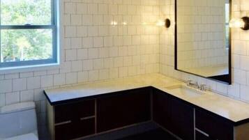 A modern bathroom with white tiles, a large mirror, a sink, and a toilet.