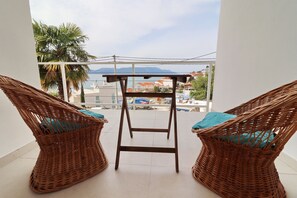 A balcony with wicker chairs and a small table, overlooking a coastal area with buildings and mountains. - Holiday Home Rosemary-Three Bedroom Holiday Home with Terrace and Partial Sea View (Klek)