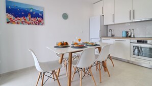 Eine moderne Küche mit weißen Schränken, einem Esstisch mit vier Stühlen und einem farbenfrohen Bild an der Wand.
