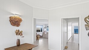 A modern interior with white walls, a wooden table, a vase with dried leaves, and a spiral metal sculpture.