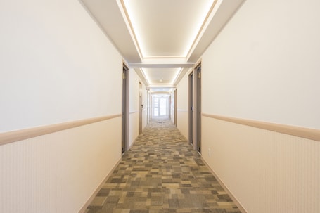 A hotel hallway with carpeted flooring, white walls, and doors on both sides.