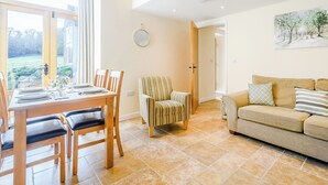 A dining area with a wooden table and chairs, a striped armchair, and a beige sofa with patterned cushions. - Pipistrelle - UK30758 (Bream, near Lydney)