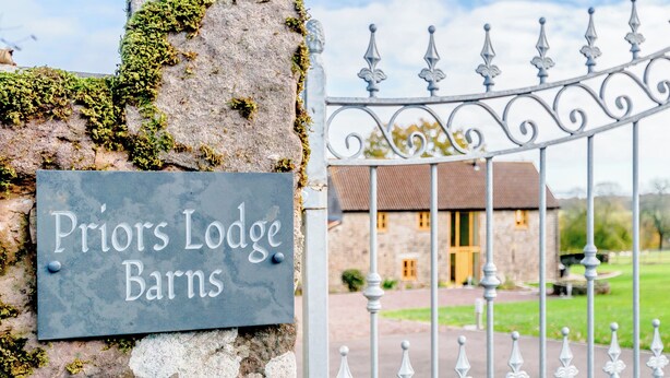 A stone wall with a sign reading "Priors Lodge Barns" and a metal gate leading to a building. - Pipistrelle - UK30758 (Bream, near Lydney)