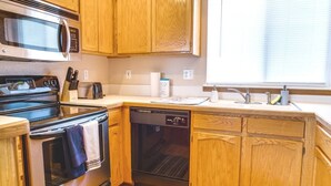 Una cocina funcional con armarios de madera, microondas, estufa, lavavajillas y una ventana con persianas.