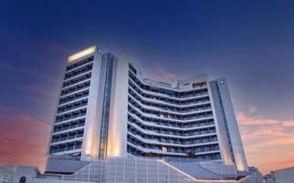 A modern hotel with multiple floors and balconies, featuring a prominent glass facade and a unique architectural design.