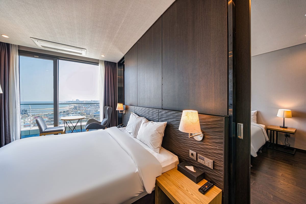 Een hotelkamer met een groot bed, een bureau, een stoel, een lamp en uitzicht op de stad.