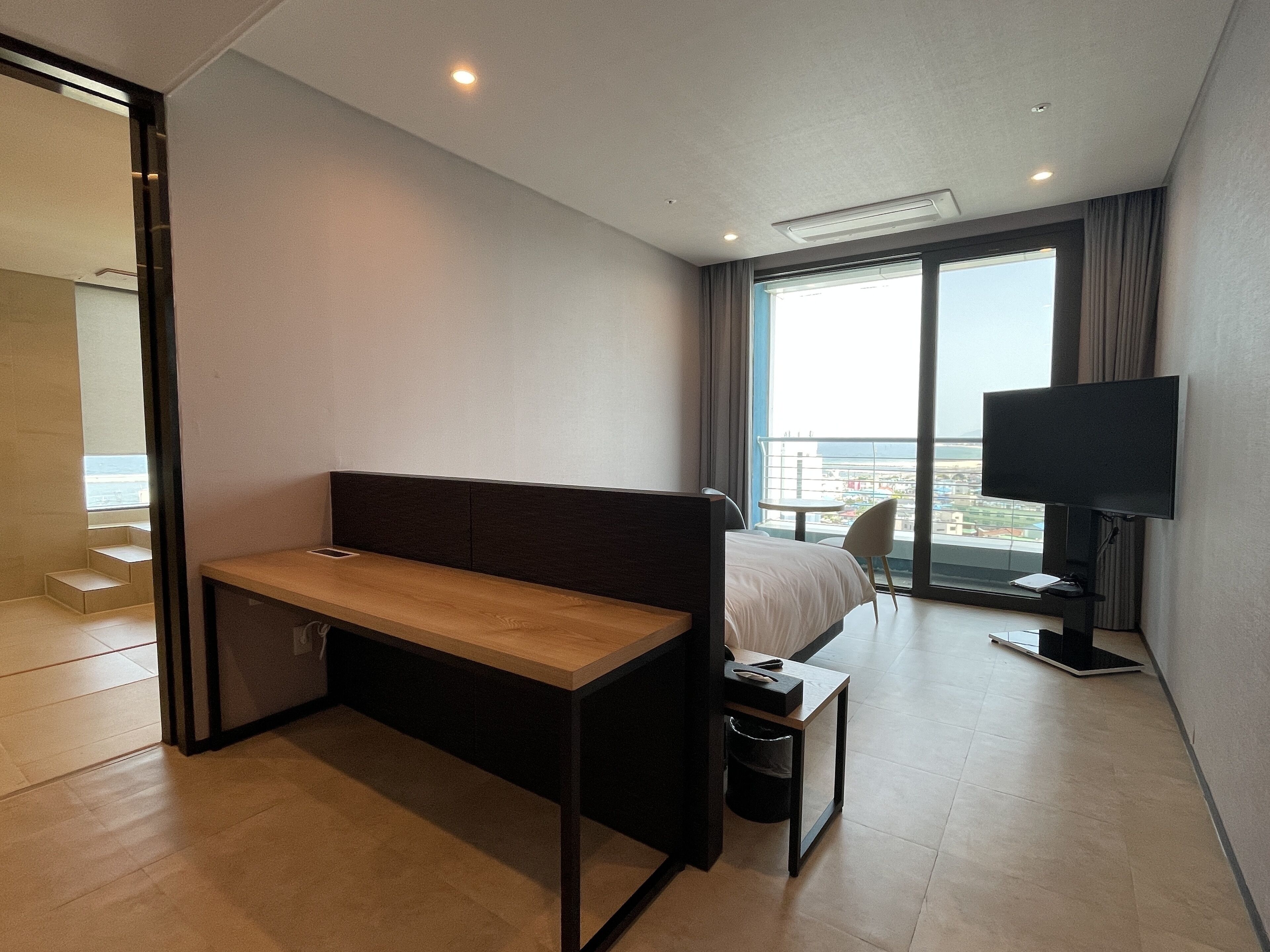 Ein modernes Hotelzimmer mit Bett, Schreibtisch, Fernseher und großem Fenster mit Blick auf die Stadt.