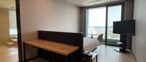 Ein modernes Hotelzimmer mit Bett, Schreibtisch, Fernseher und großem Fenster mit Blick auf die Stadt.