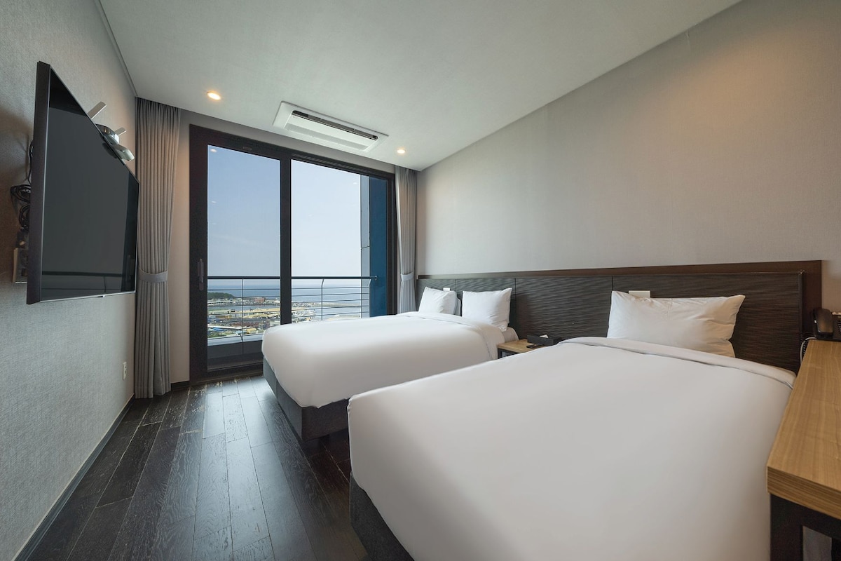 Habitación de hotel con dos camas, televisor y vistas a la ciudad.