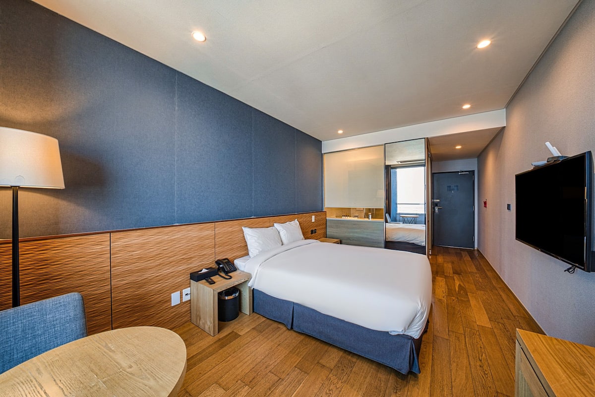 Een moderne hotelkamer met een groot bed, nachtkastje, lamp en een televisie.