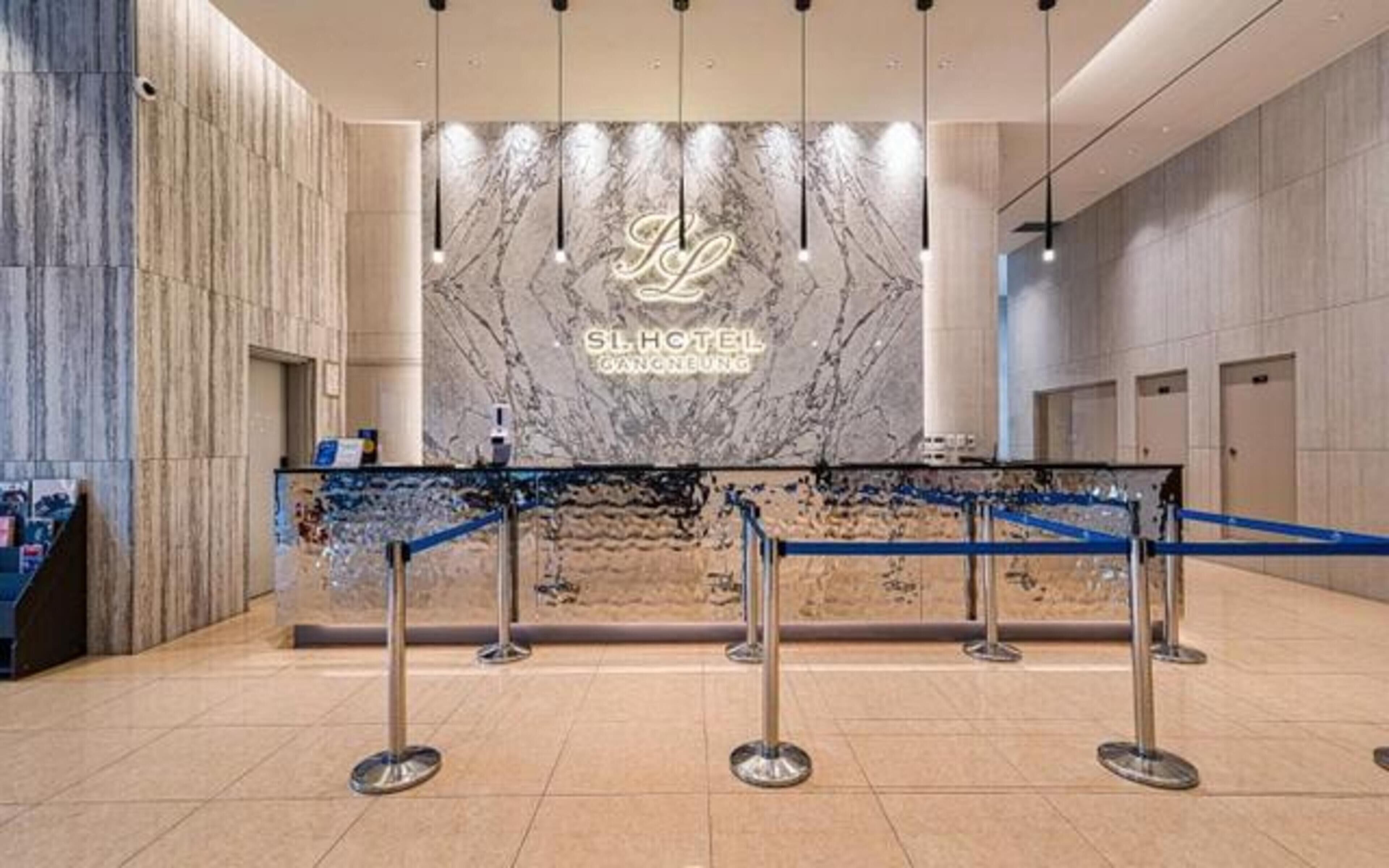 Zona de recepción de un hotel con pared de mármol, mostrador de recepción y una barrera azul.