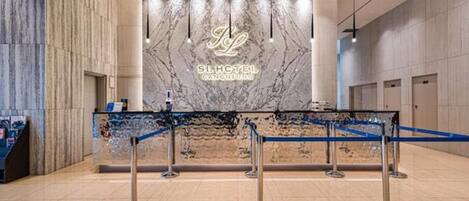 Zona de recepción de un hotel con pared de mármol, mostrador de recepción y una barrera azul.