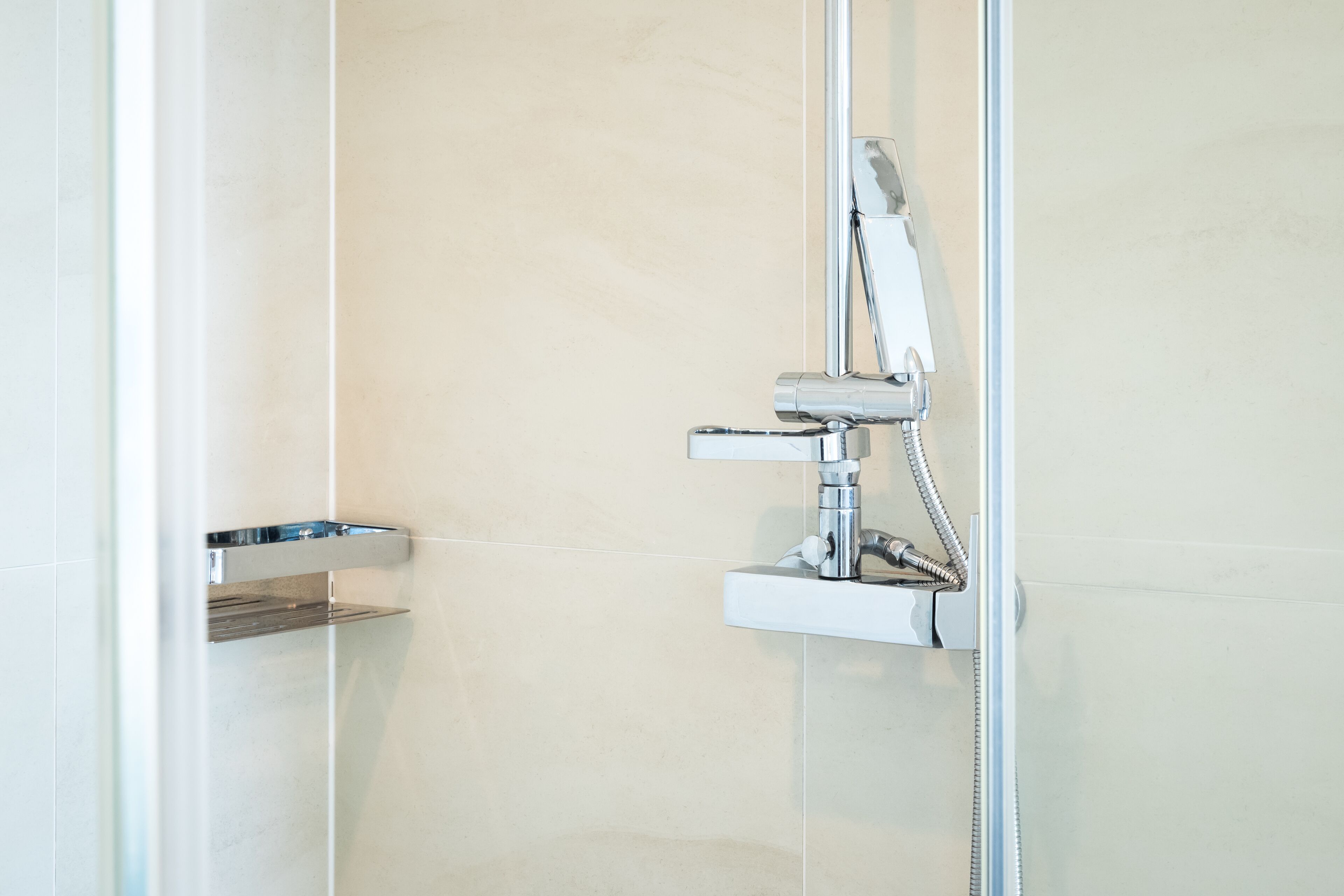 A modern bathroom with a chrome showerhead and a small shelf.