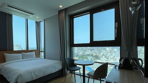 A hotel room with a bed, a small round table with two chairs, a remote control, and large windows offering a city view. - SL Hotel Gangneung (Gangneung)