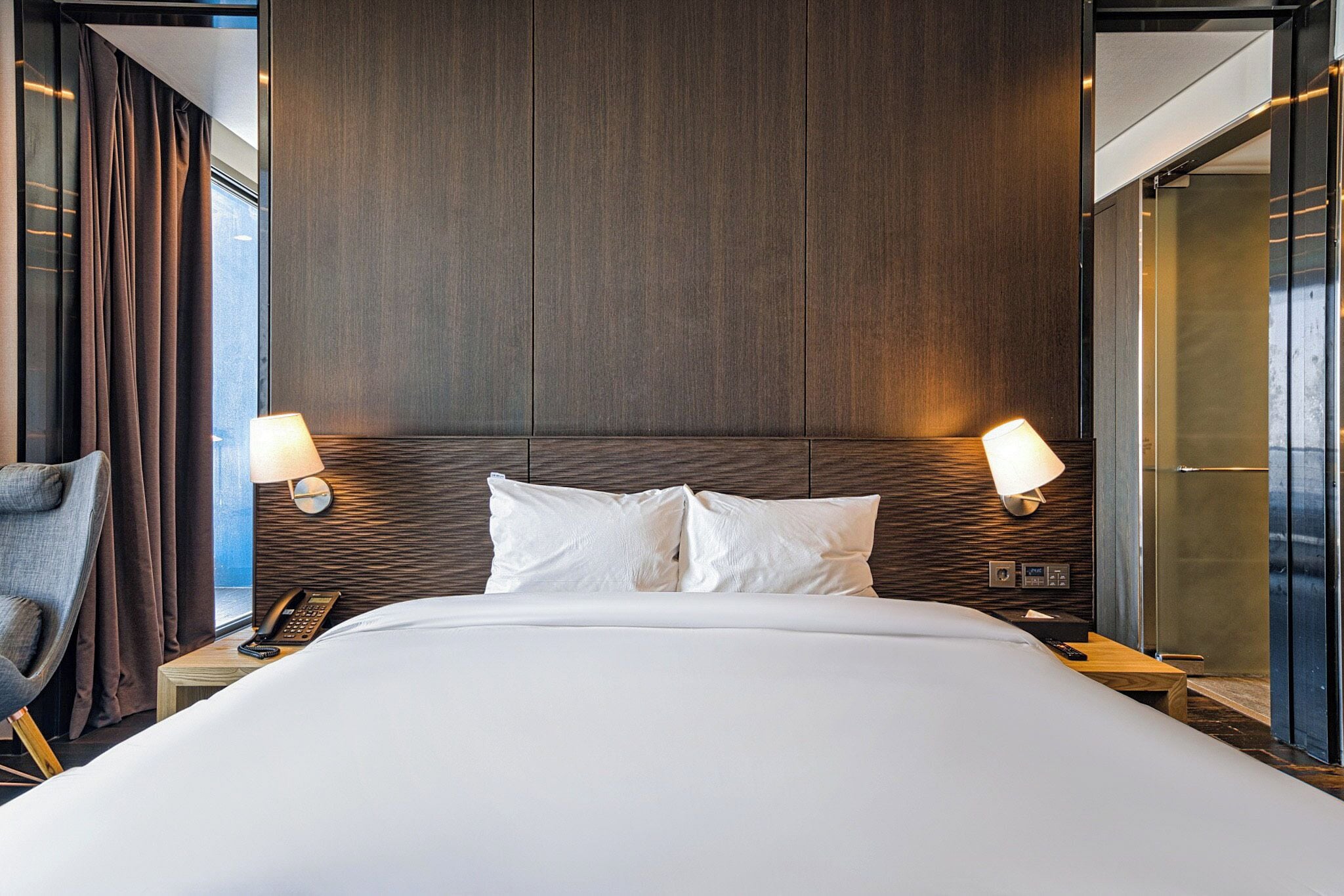 A modern hotel room with a large bed, two bedside lamps, a telephone, and a chair.