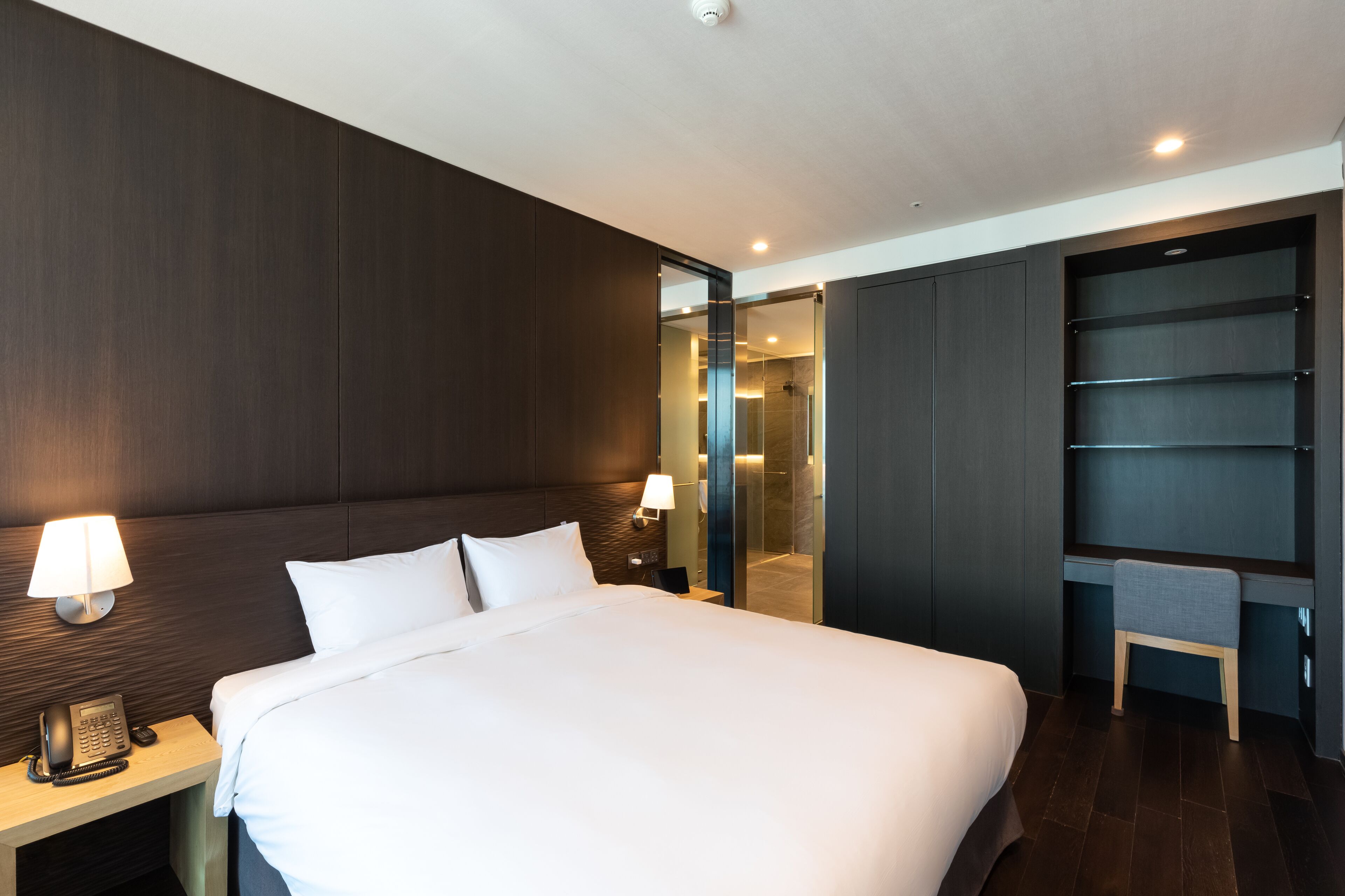 Une chambre d’hôtel moderne avec un grand lit, des lampes de chevet, un téléphone et une douche séparée par une paroi en verre.