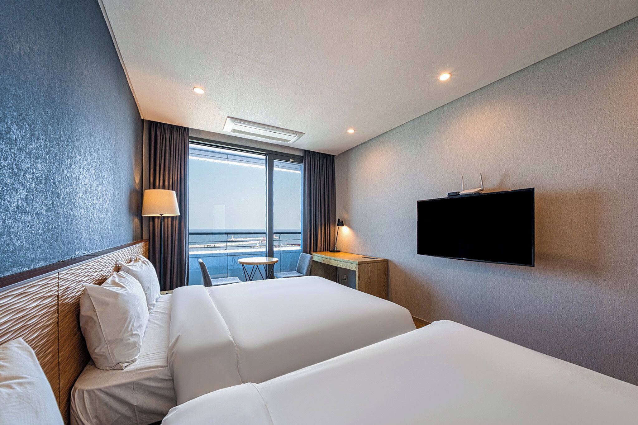 Een hotelkamer met twee bedden, een bureau, een televisie en uitzicht op zee.