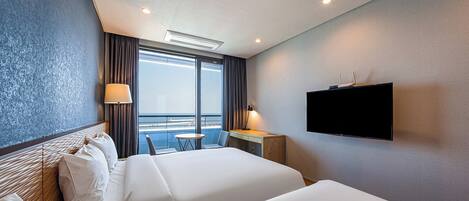 Een hotelkamer met twee bedden, een bureau, een televisie en uitzicht op zee.