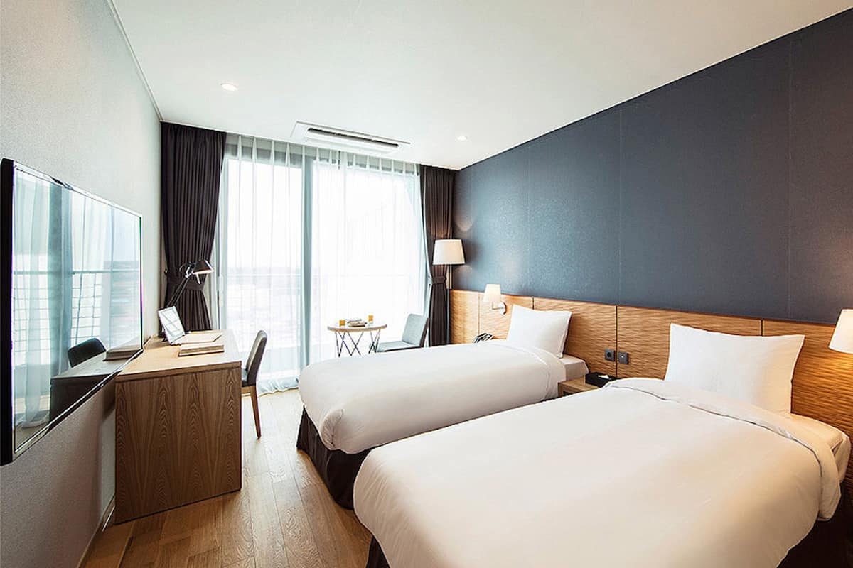 Een hotelkamer met twee bedden, een bureau, een stoel, een televisie en een raam met gordijnen.