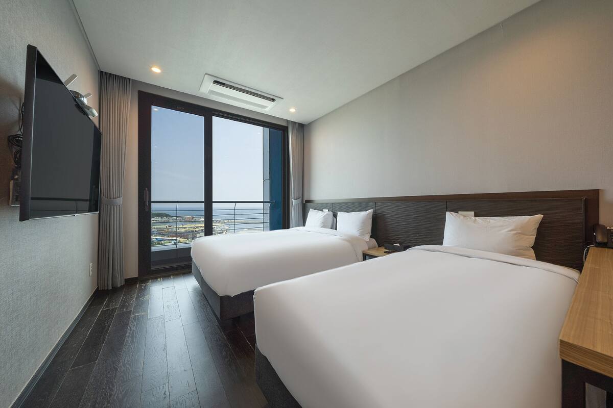 Een hotelkamer met twee bedden, een televisie, een groot raam en een balkon.