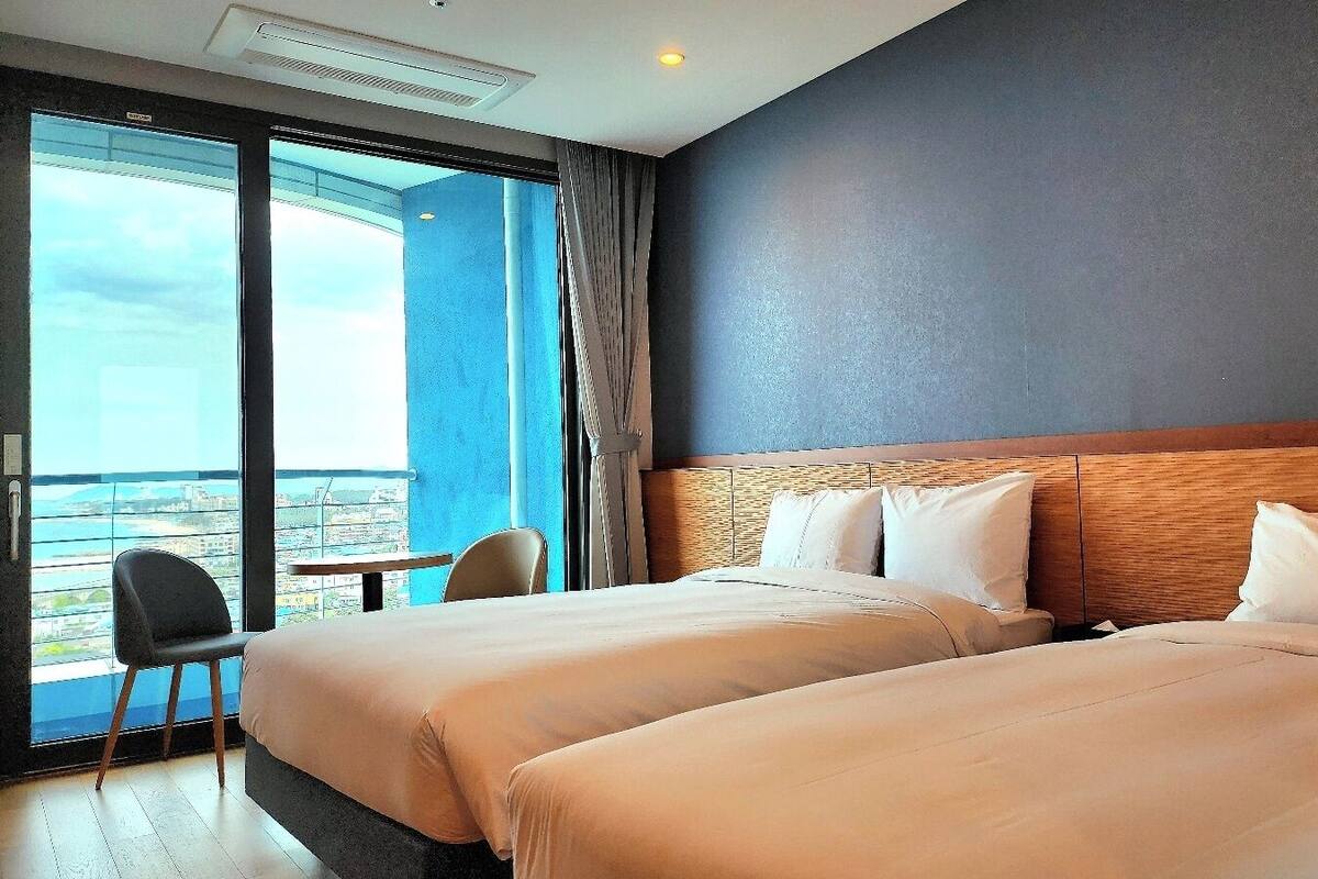 Een hotelkamer met twee bedden, uitzicht op de stad en een stoel bij het raam.