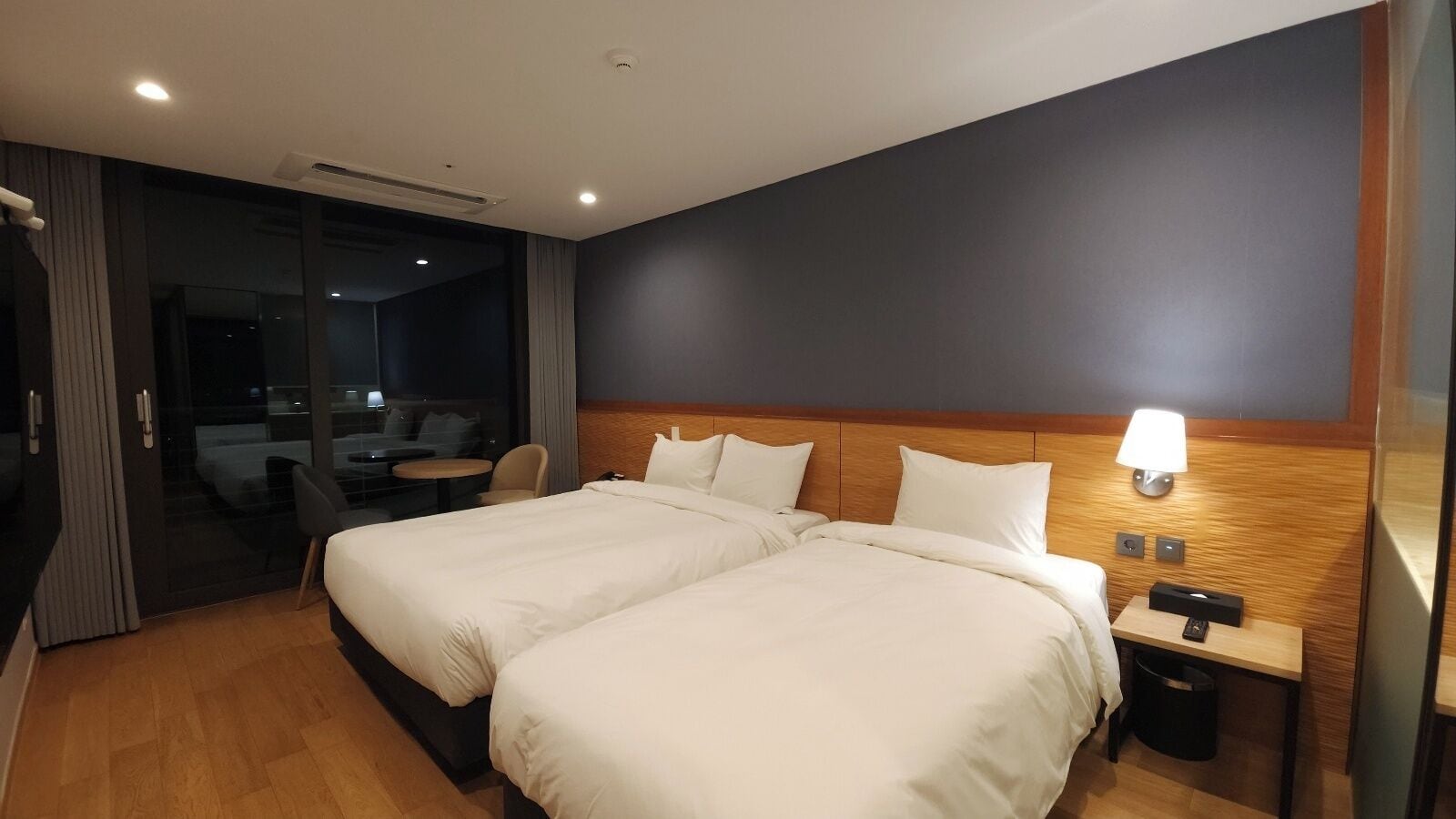 Een hotelkamer met twee bedden, een bureau, een stoel en een glazen schuifdeur naar een balkon.