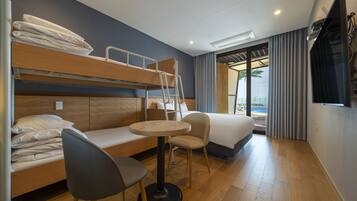Habitación de hotel con literas, una mesita redonda pequeña, una silla, una cama, un televisor y una ventana con cortinas.