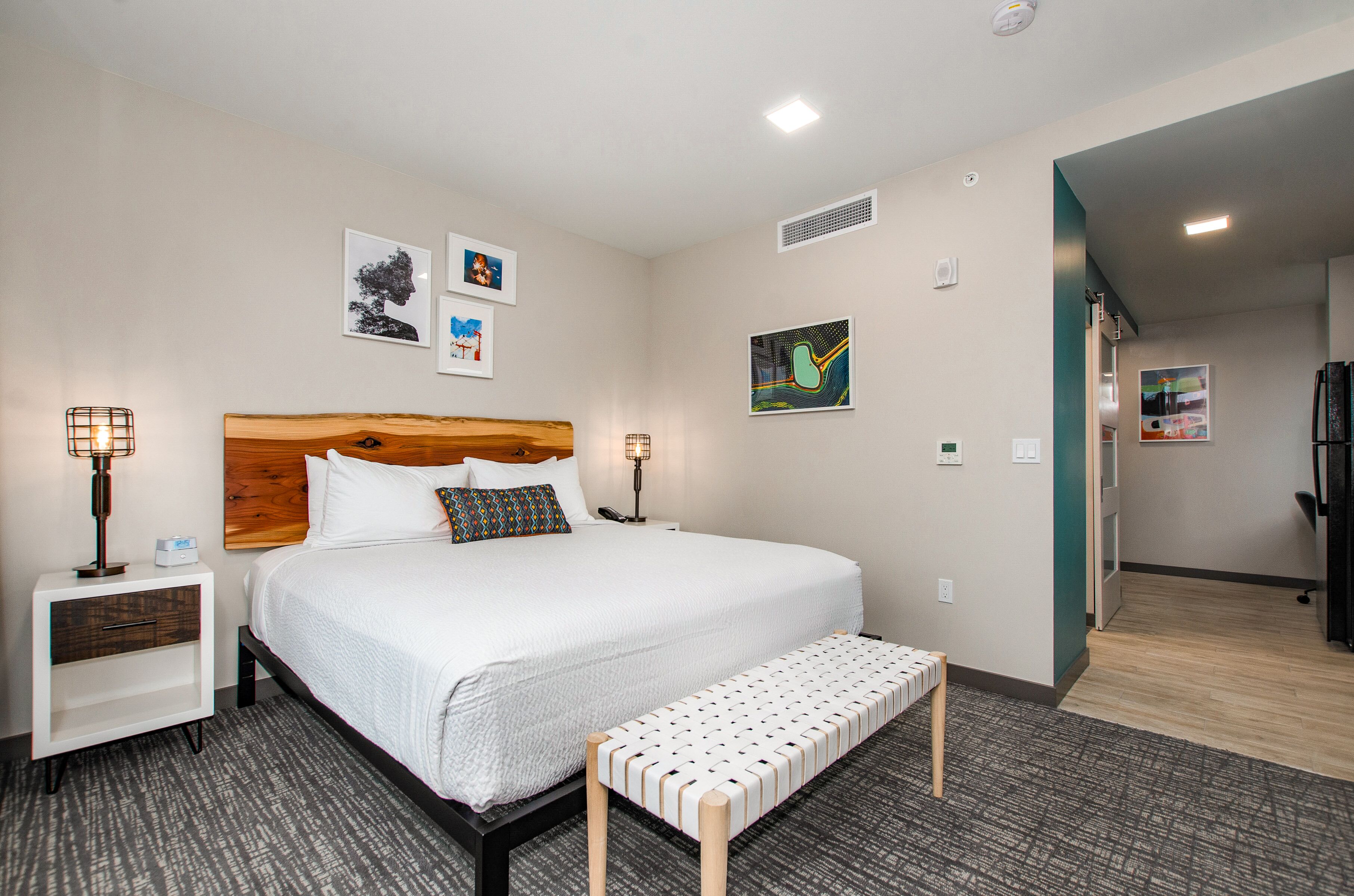 A hotel room with a large bed, bedside tables, a bench, and artwork on the walls.